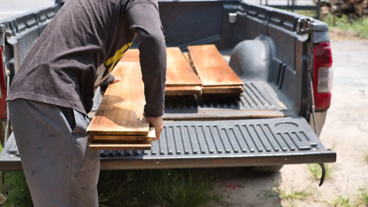 Carpenter uploading pile of lumber woods and palnks on to pick up truck. Woodworking concept.