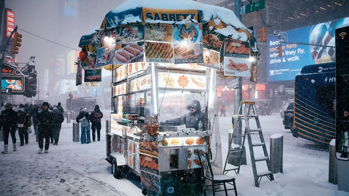 A man works in a food cart during a snowstorm.