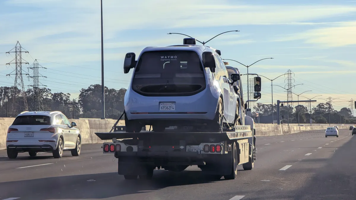 A blue vehicle on a flatbed truck along a highway with other cars.