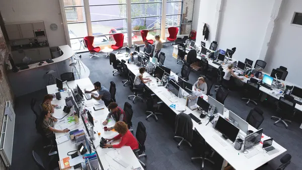 A large office seen from above with workers at multiple open workstations.