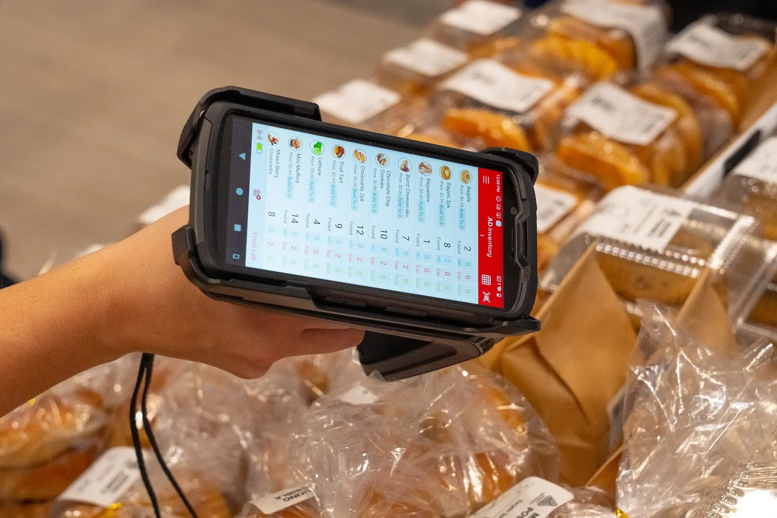 A person's hand holds a digital scanner with various food items listed on the screen.