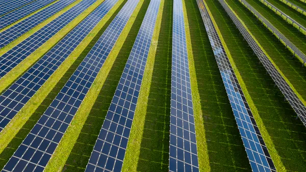 Rows of solar panels are seen against a green field.