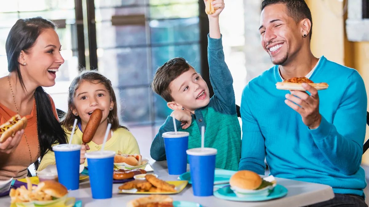 A family of four eating pizza, corn dogs and other fast food items.