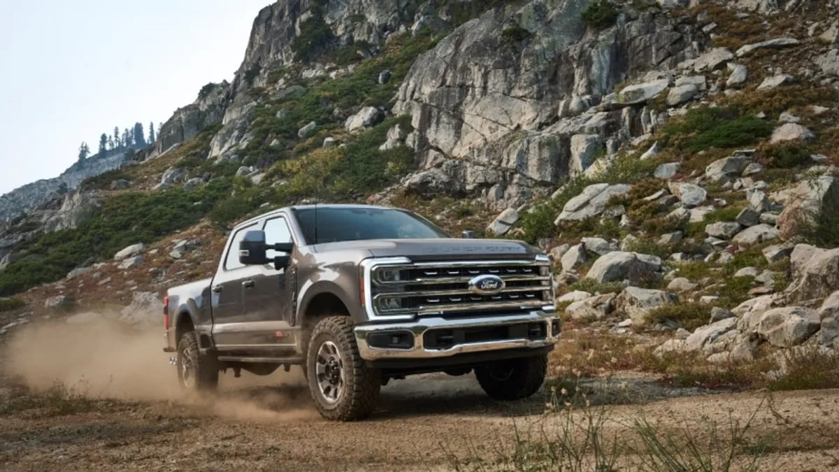 A 2024 Ford F-Series Super Duty driving off road outdoors with large boulders in the background.