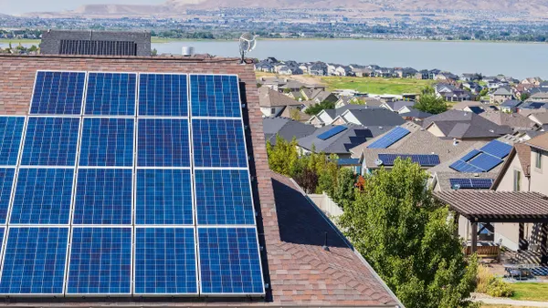 Rooftop solar panels installed on a suburban home, with a neighborhood full of houses and mountains in the background under a sunny sky.