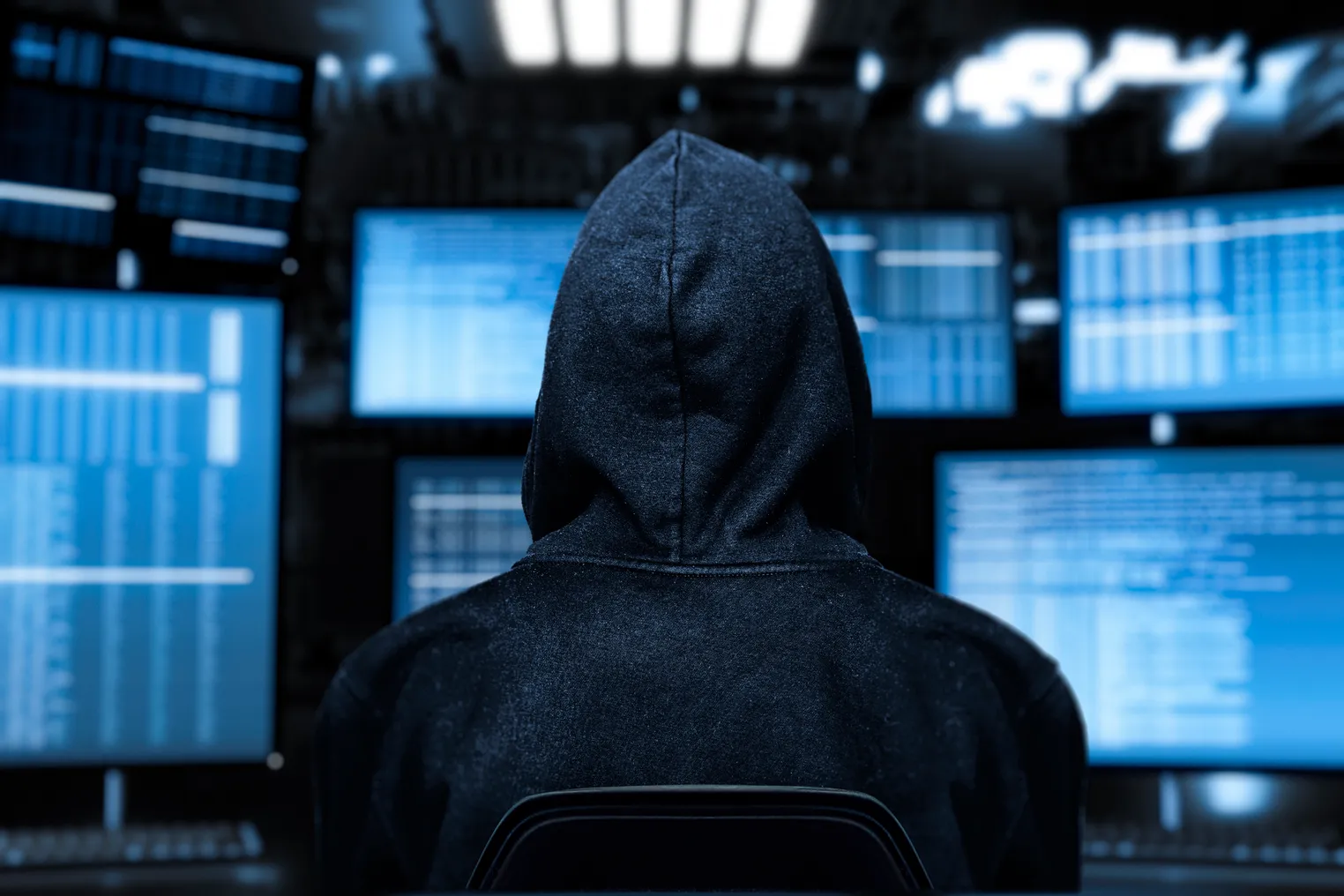 Image of a hacker facing a computer screen with blue text