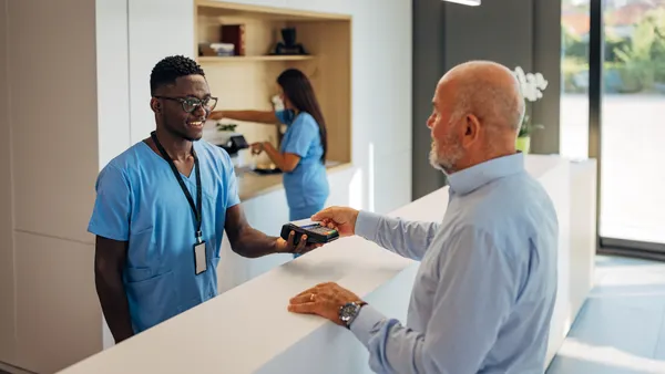 Senior male patient pays for medical services with a credit card at the clinic reception