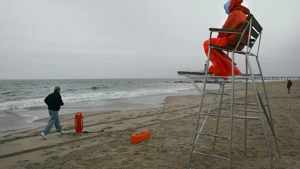 A person jogs along a rainy beach past a lifeguard.