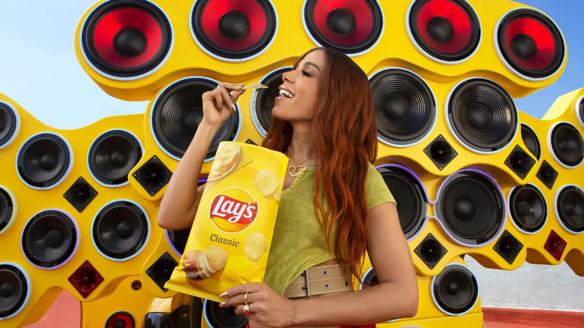 Brazilian singer Anitta holds a Lay's chip in front of a giant speaker display