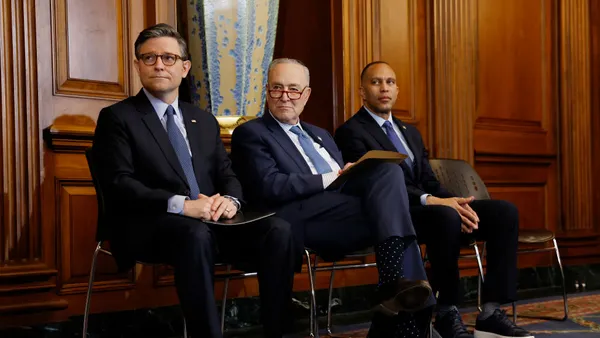 Three people in suits and ties sit in chairs at a Congressional event