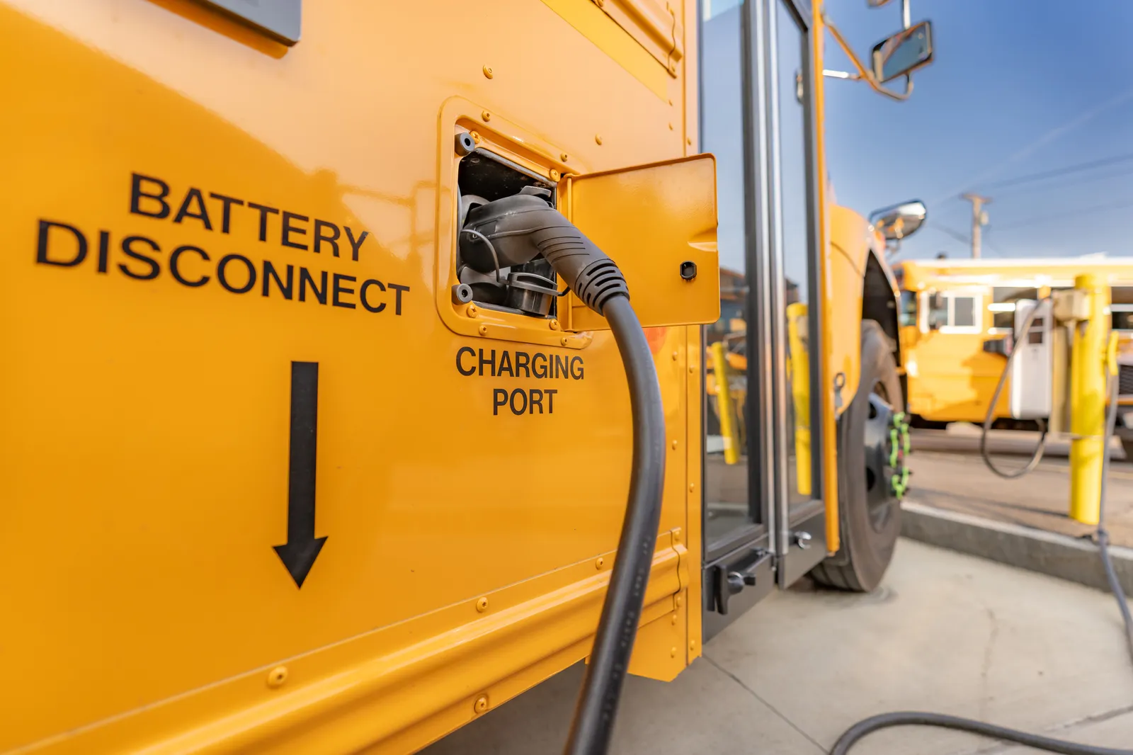 A yellow electric school bus is plugged in at a charging station.