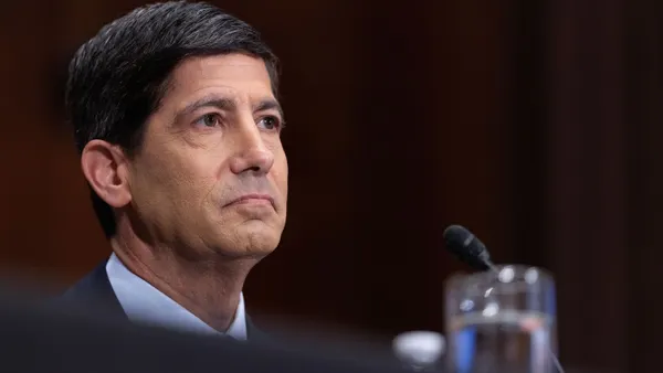 A close-up of a person wearing a suit and tie, listening during a committee hearing.