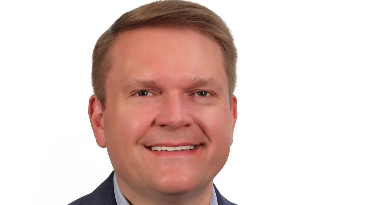 A photograph of a person wearing a suit and smiling.