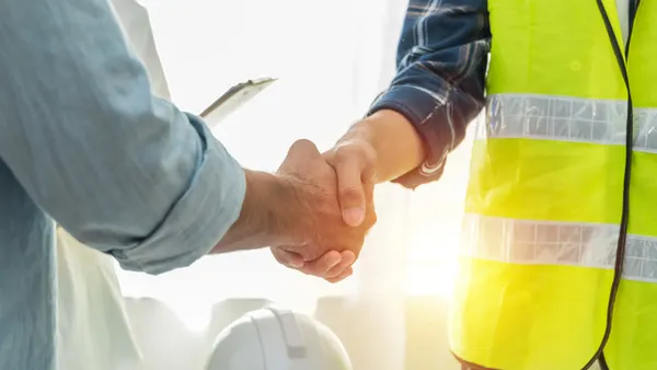 Two people, one in a construction vest, shake hands.