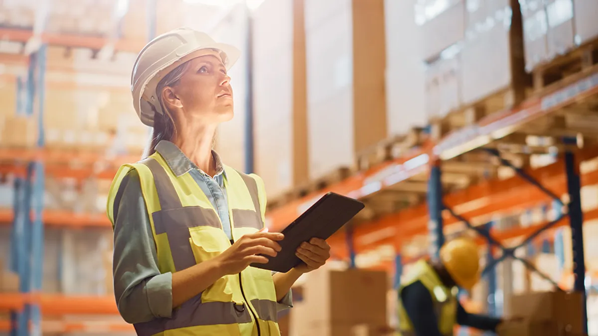 A construction worker holding a tablet and looking up in a warehouse