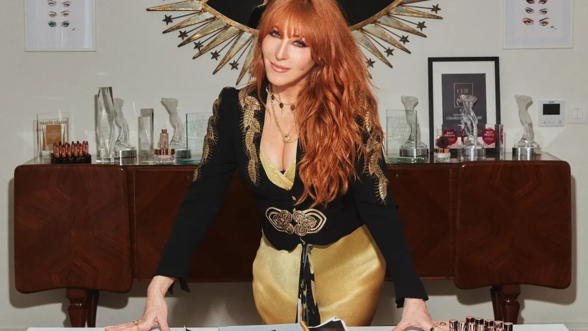 A person with long red hair leans on a table.