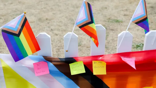 Notes are affixed to a pride flag that hangs on a fence.