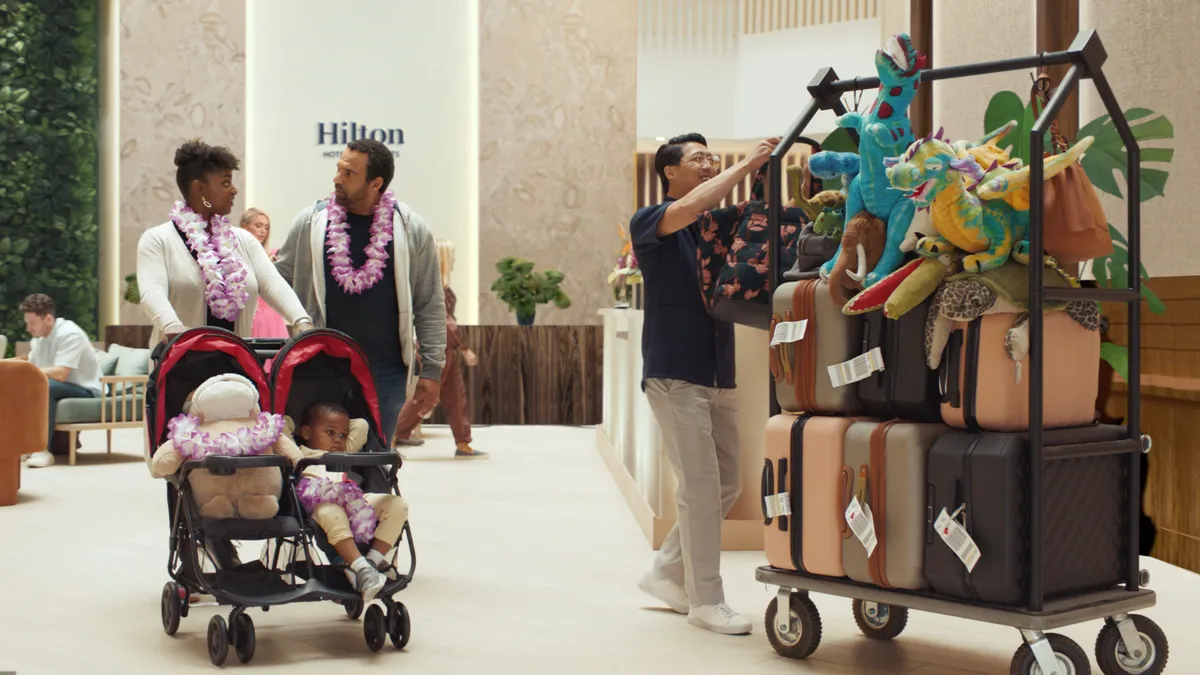 A couple and their kid walk through a Hilton hotel lobby while pushing their child in a stroller.