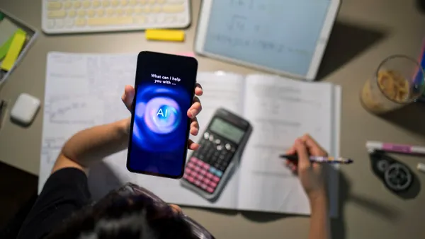 A student interacts with an AI chatbot on a cellphone while studying with a calculator, notebook, and digital tablet on a desk.