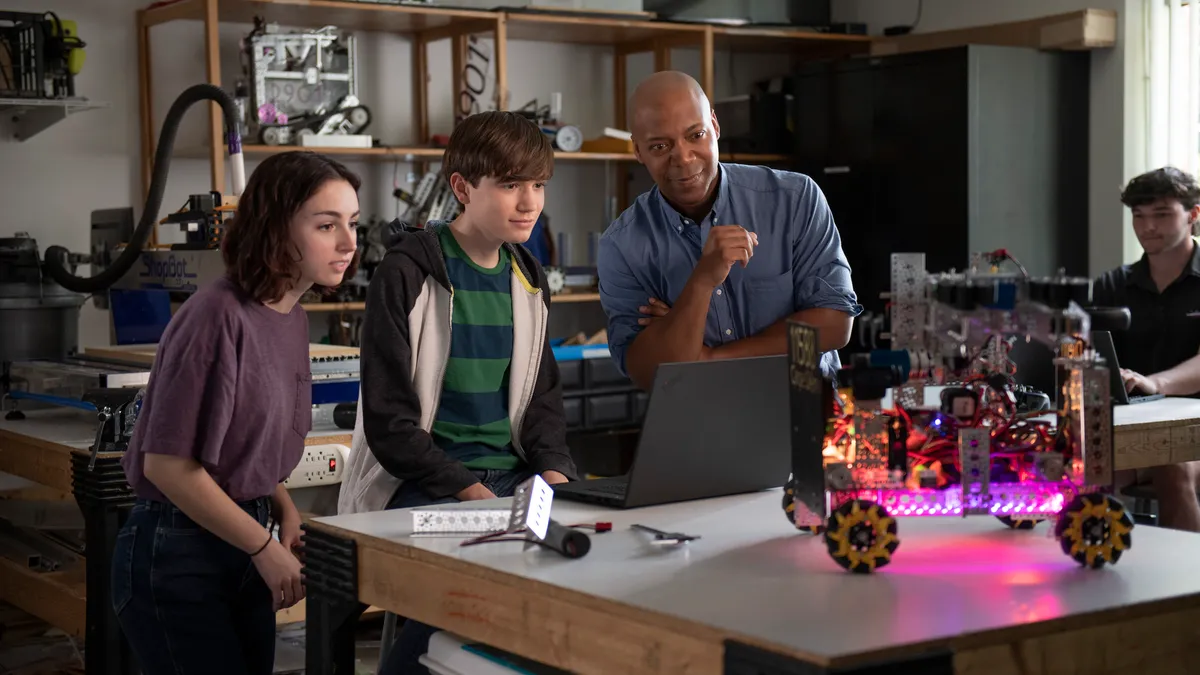 Three people looking at an open laptop