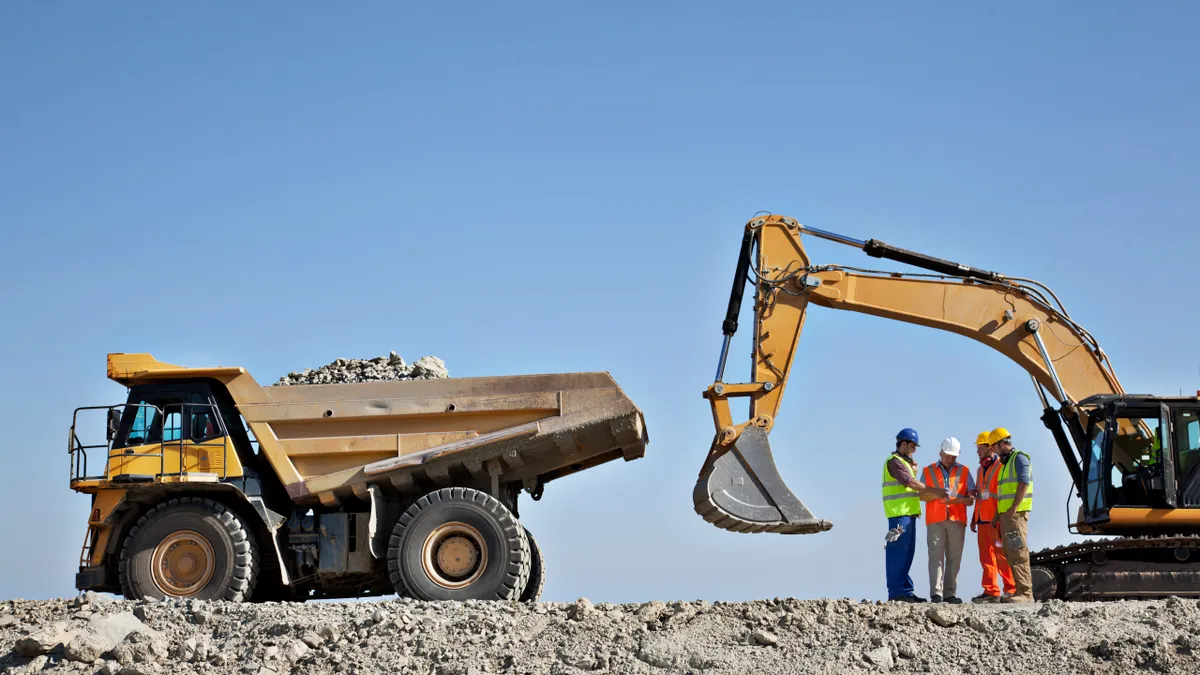 Workers talking by machinery in quarry - stock photo