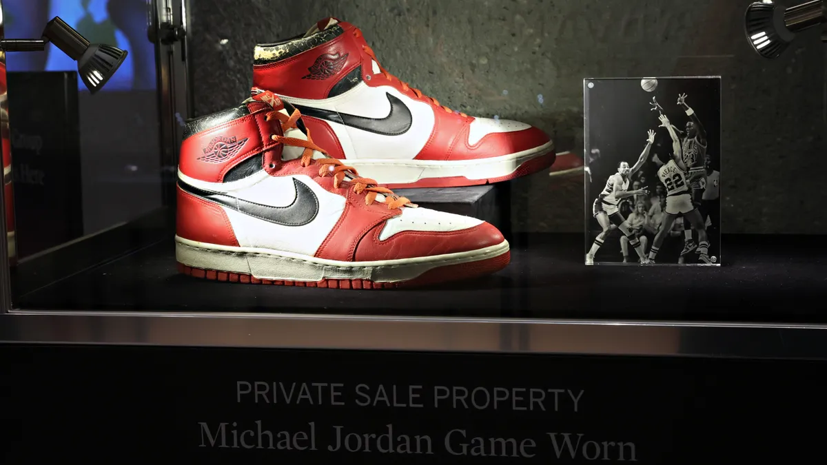 Nike red, black and white Air Jordan 1 "Dunk Sole" shoes are displayed in a glass case alongside a photo of Michael Jordan wearing them in a game.