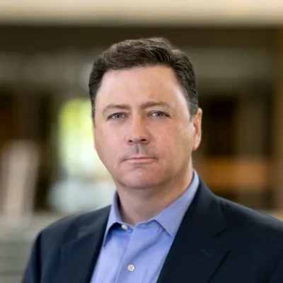 A headshot of Shawn Millerick wearing a black suit with a blue shirt.