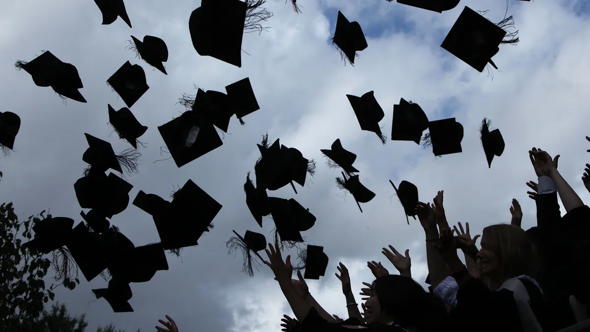 The silhouette of dozens of gowned students throwing their graduation mortarboards in the air is shown against a bright blue sky as they celebrate, a portend of the bright future that lay ahead.