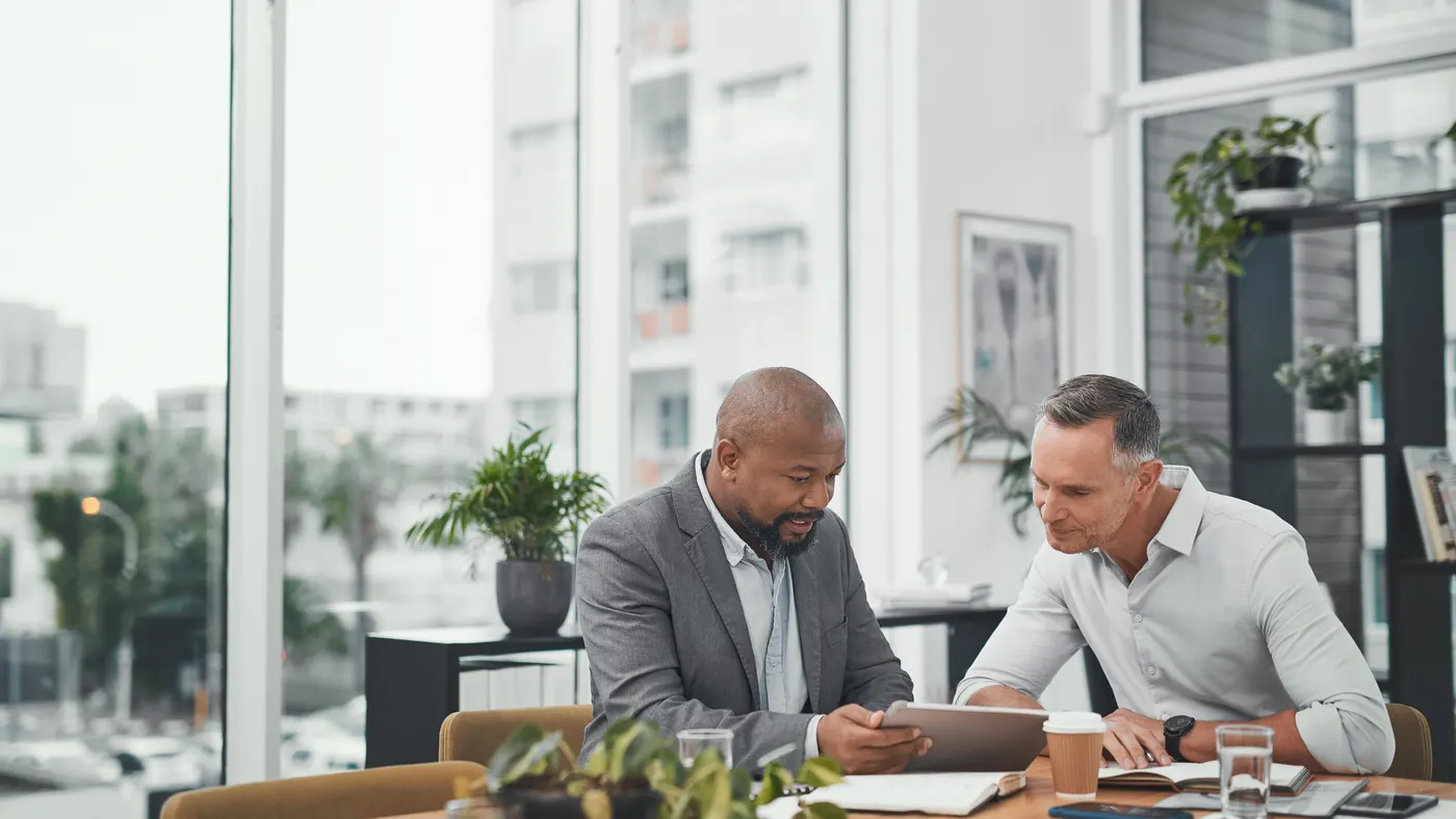 Two people using a digital tablet during a meeting in a modern office.