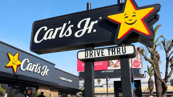 An image of a black sign with a yellow star and workding that says Carl's Jr drive thru