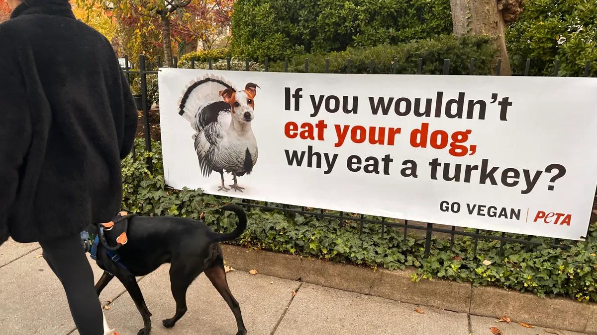 A person and their dog walk past a sign on PETA's gate that reads "If you wouldn't eat your dog, why eat a turkey?"