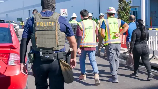 A group of construction workers walk accompanied by law enforcement.