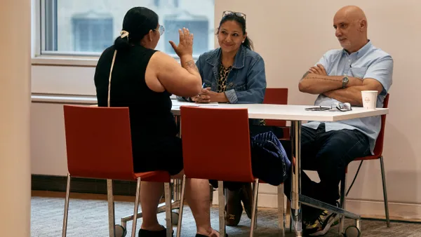 An individual engaged in conversation sits at a table across from two others.