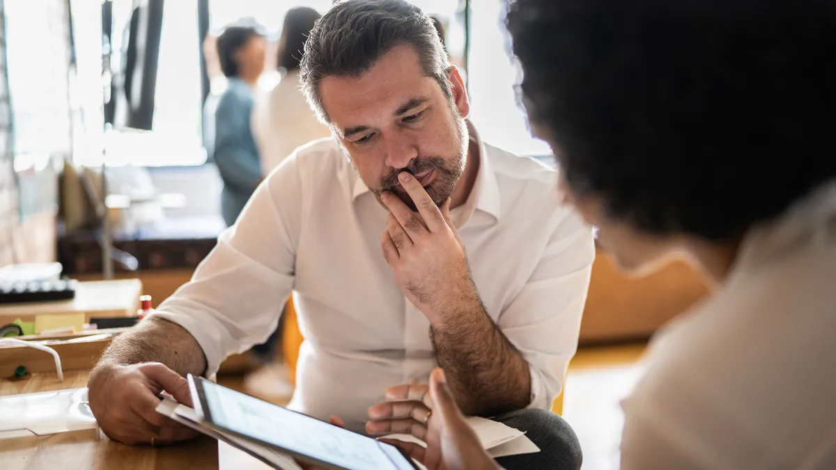 Mature man looking at a digital tablet that a colleague is showing at work.