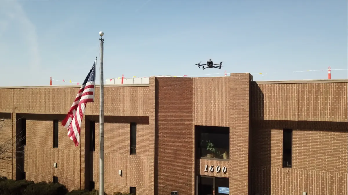 A drone flies over a brick building with 1600 over the door and U.S. flag on flagpole in front.
