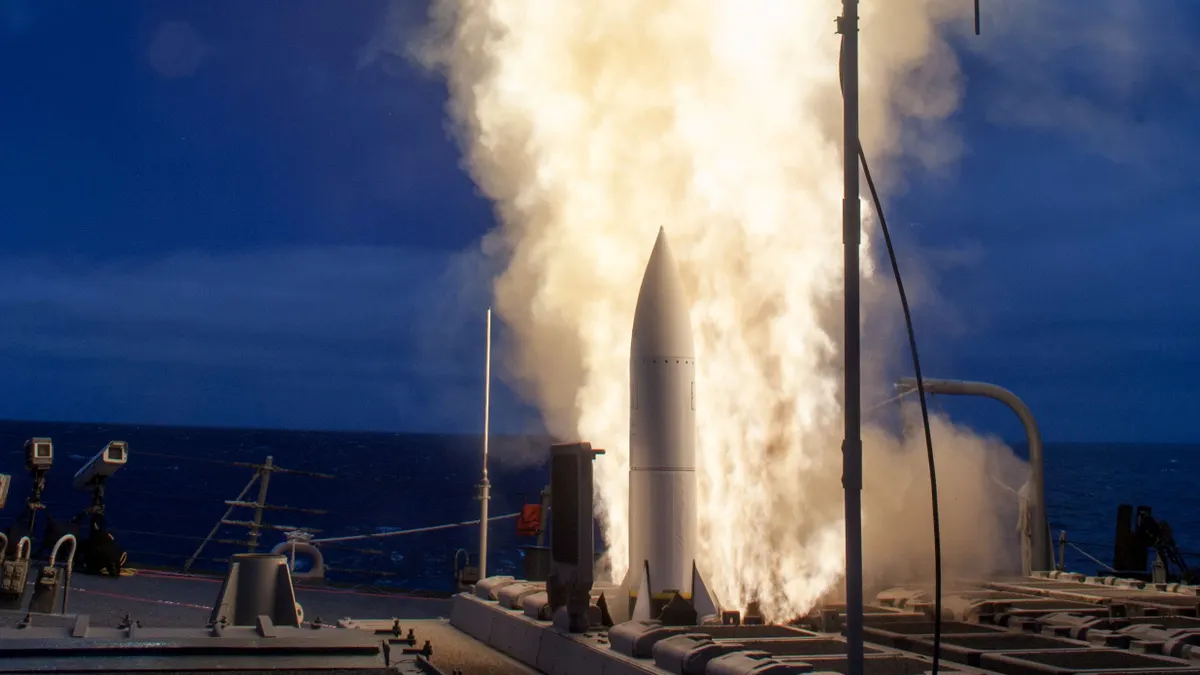 A missile fired up to launch from a deck of a ship at night.