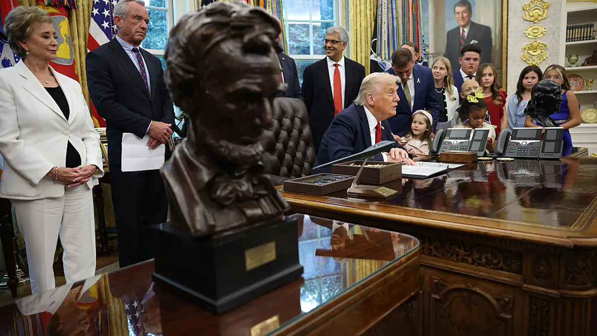 One person is seated at a desk while several adults and children are gathered around. A bust of Abraham Lincoln is in the foreground