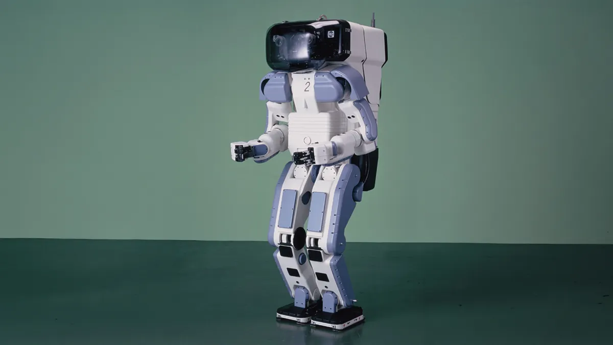 A white and blue humanoid robot stands in an empty forest green room