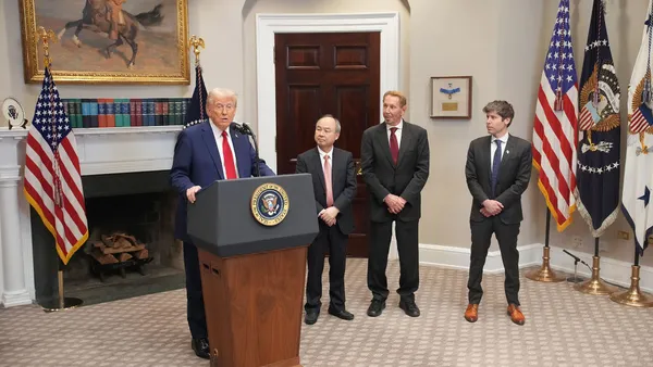 President Trump speaks at a lectern bearing the presidential seal, flanked by three executives