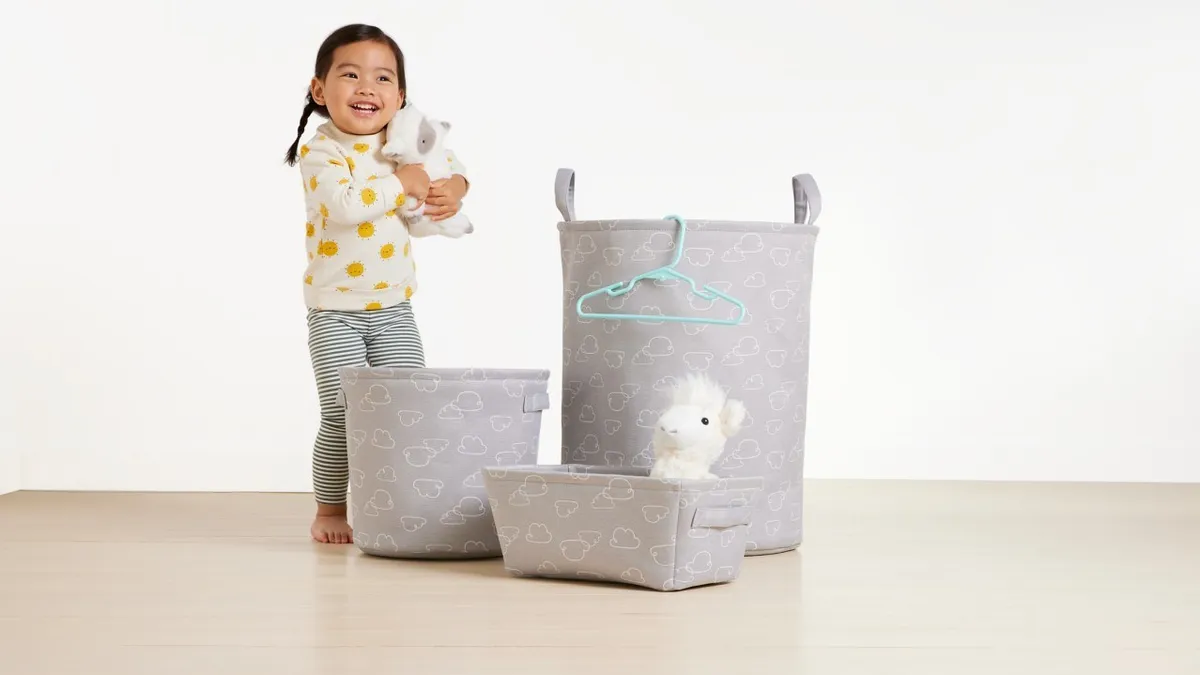 A girl holding a stuffed animal standing behind three storage bins