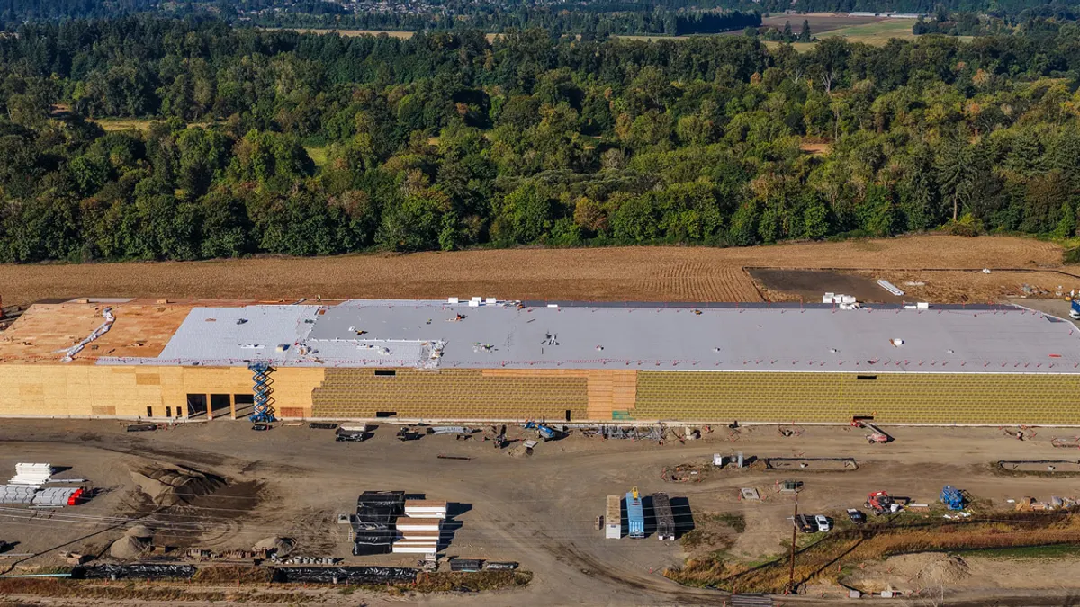 A far-out skyshot of a large facility that sits on a new construction site. The long building stretches to the edge of the frame.