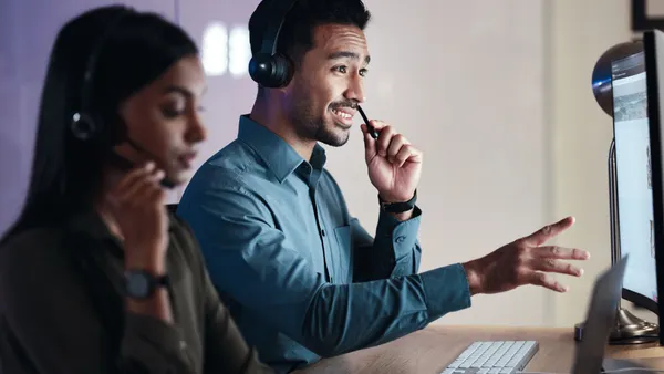 A contact center agent with a headset gestures at a computer screen.