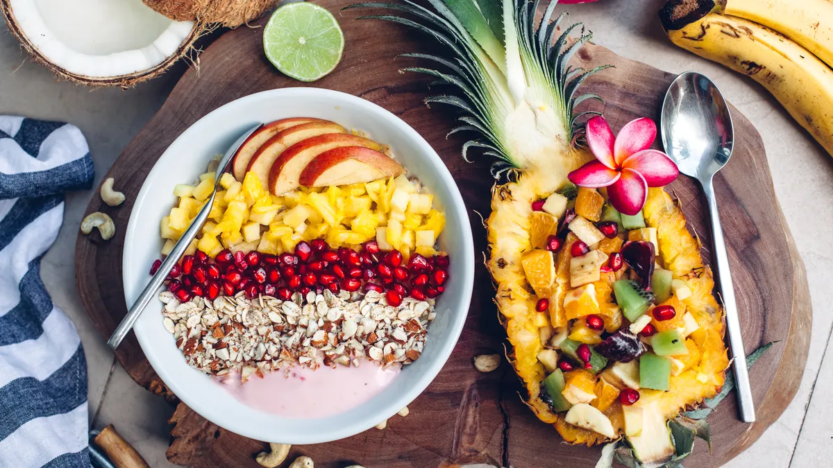 Smoothie bowl with colorful tropical fruits on wooden serving tray, top view from above.