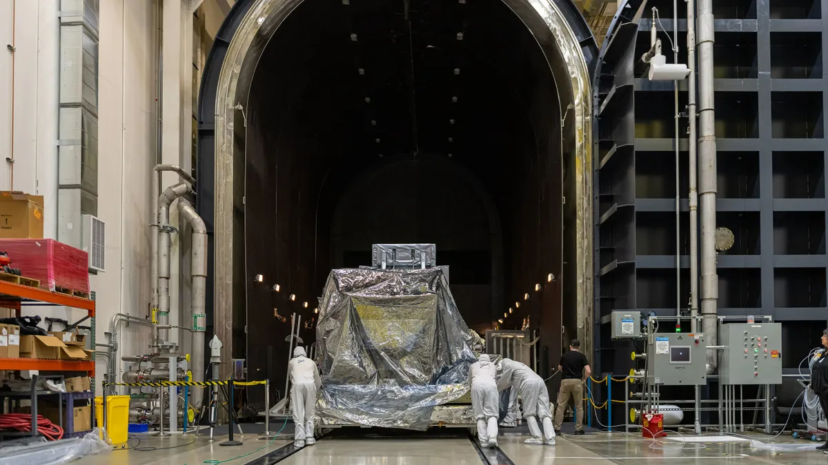 Three people in full-coverage protective suits push a piece of aerospace equipment.