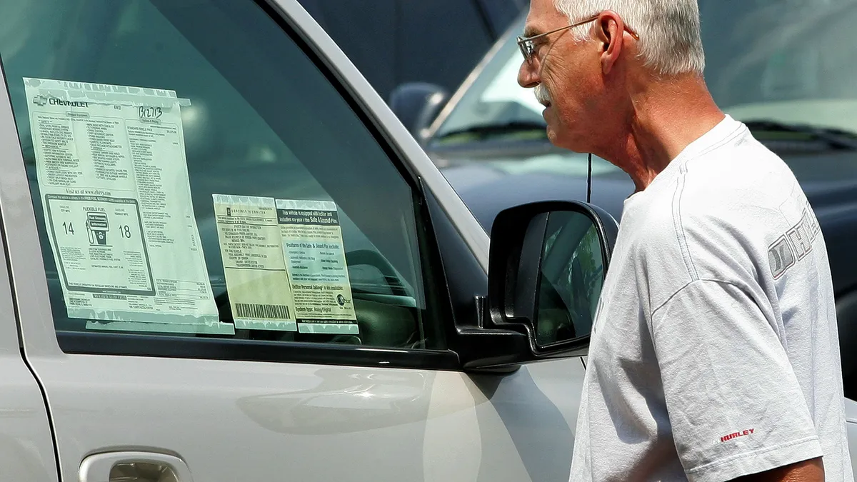 Consumer looks at window sticker on car with pricing information.