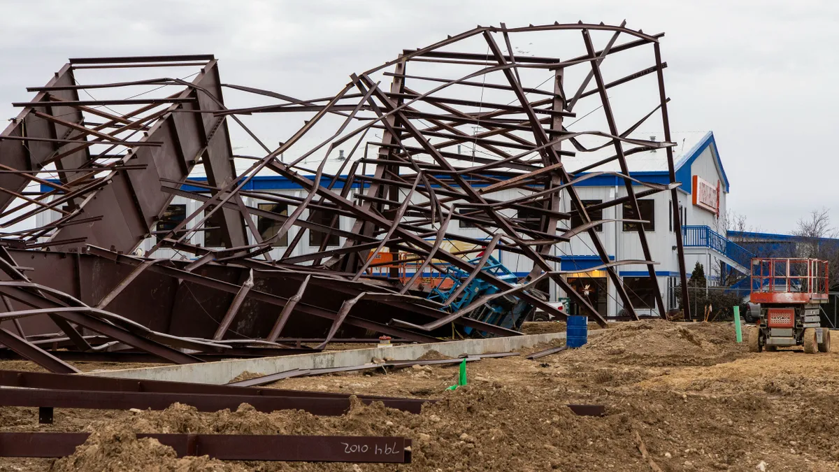 The frame of a structure under construction sits broken and twisted, collapsed on a jobsite.