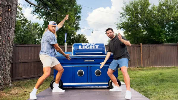 George Kittle and Baker Mayfield pose with a Traegerator in a backyard.