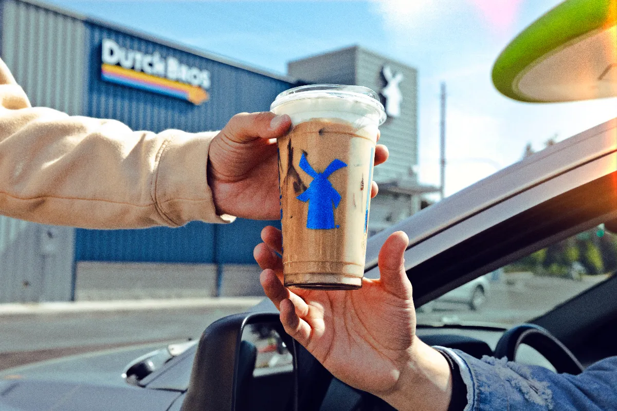 A picture of a hand giving a iced coffee drink to another person.