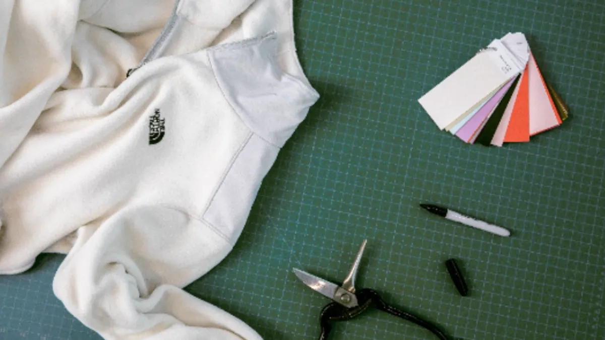 A North Face top is on a worktable with pliers, color swatches and a marker.