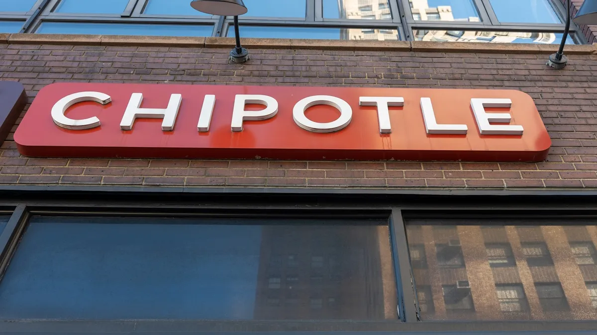 A photograph of a brick building with a red sign and white letters that says Chipotle.